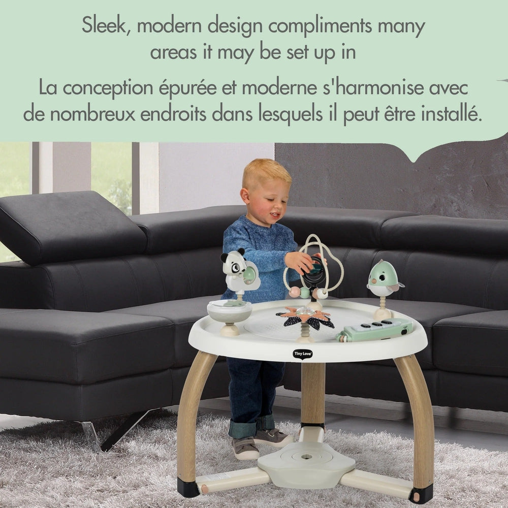Tiny Love 5-in-1 Here I Grow Stationary Activity Center; child plays with hanging toys on a white round table with wooden legs.