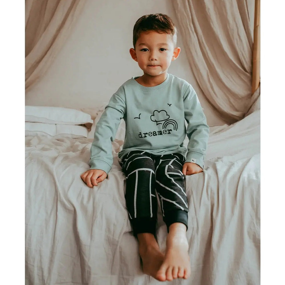 Turtledove London Geo Jacquard Harems: toddler sits on a bed in a teal top with dreamer graphic and black geometric harems.