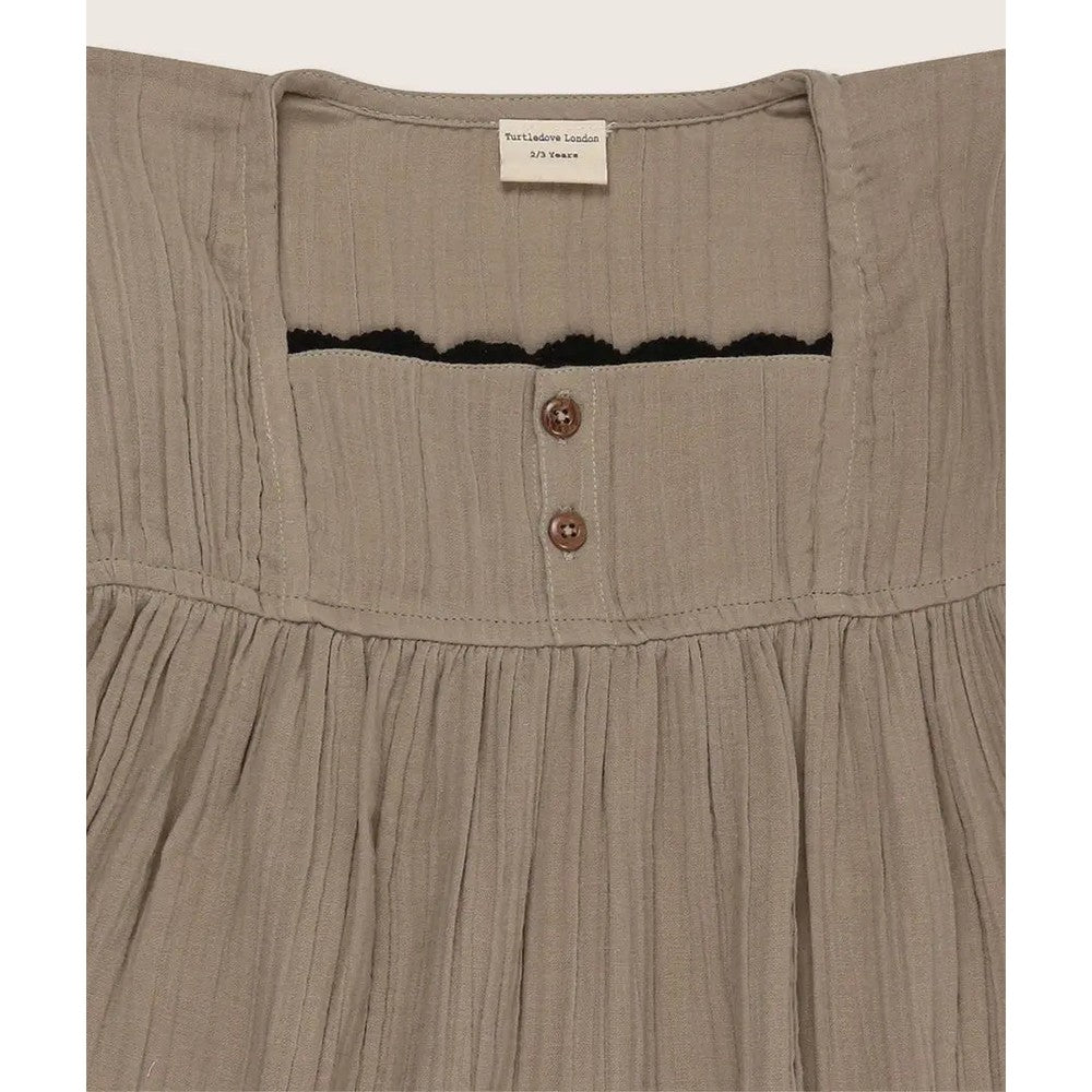 Turtledove London Herb Gauze Dress for toddlers, beige gauze fabric with brown back buttons and black trim.