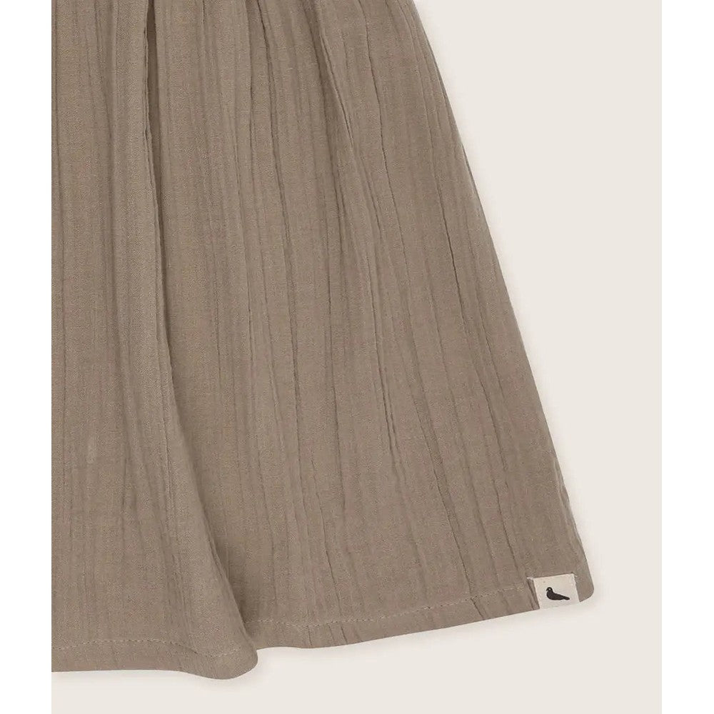 Turtledove London Herb Gauze Dress for babies in taupe gauze, lightweight pleated fabric with a small brand tag at the hem.