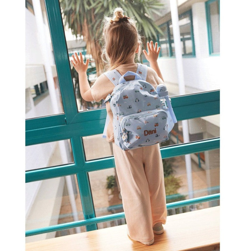 Tutete children's backpack in light blue with a playful print worn by a toddler in a beige jumpsuit