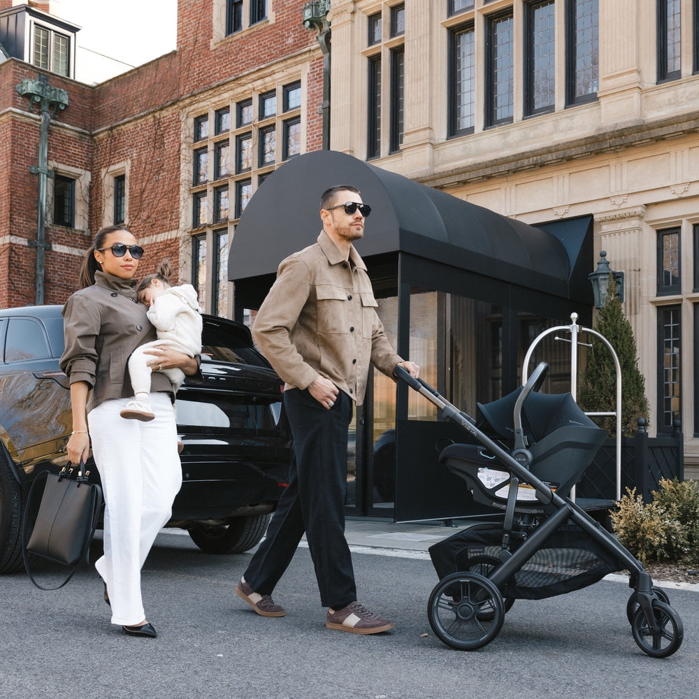 Two adults pushing a stroller in front of a building with a car in the background