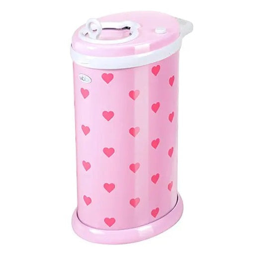 Ubbi Ubbi Diaper Pail in pink with red hearts and white lid, standing upright in a nursery.