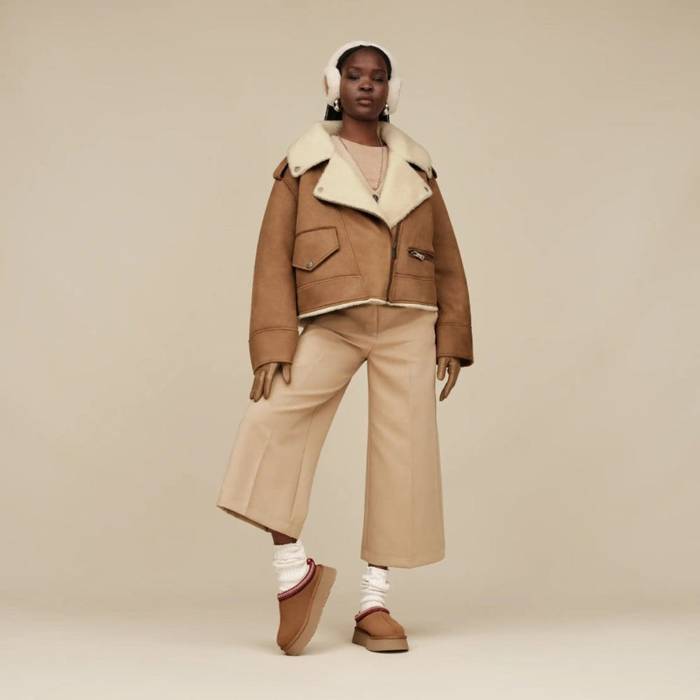 UGG Women's Tazz II Chestnut boots with plush shearling lining, as the model strides in tan wide-leg pants.