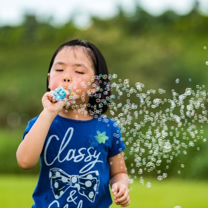 Uncle Bubble Foamy Bubble toy; child blowing bubbles outdoors in a blue shirt.