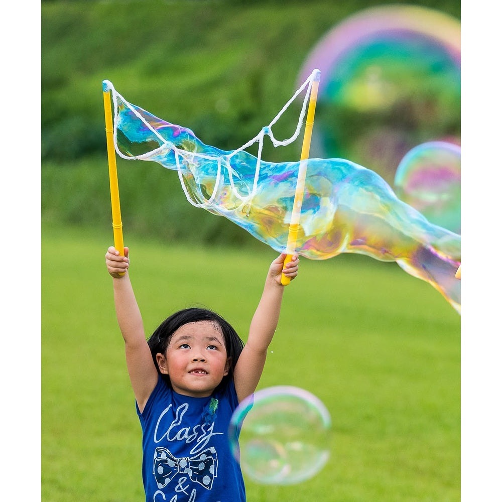 Uncle Bubble Giant Wizard bubble wand with 4 oz solution; child outdoors blowing colorful bubbles.