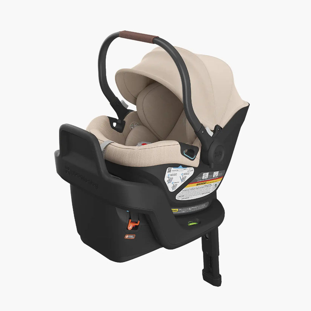 Uppababy Aria Car Seat in beige fabric with black base and curved brown-grip handle for easy transport.