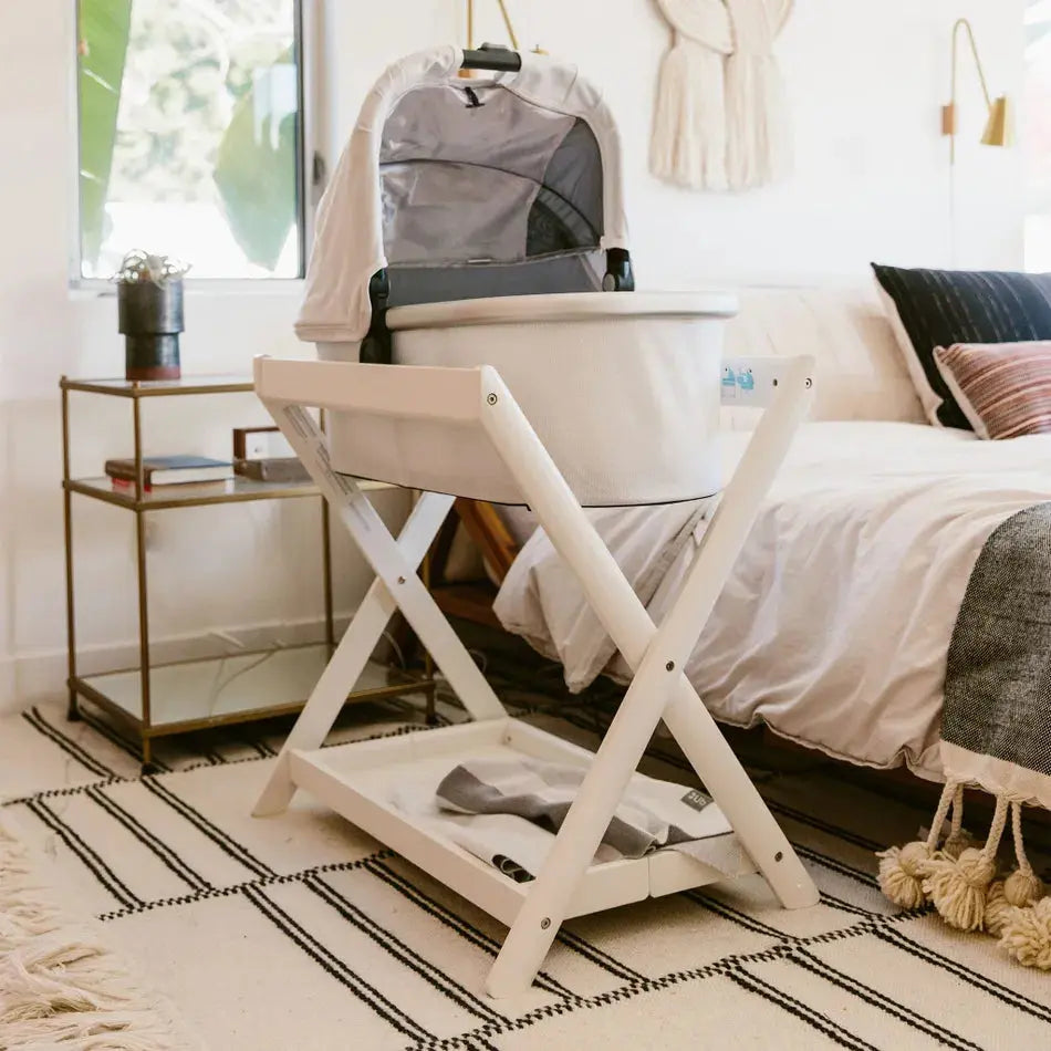 UPPABABY Bassinet Stand with white wooden frame supporting a gray bassinet in a cozy nursery.