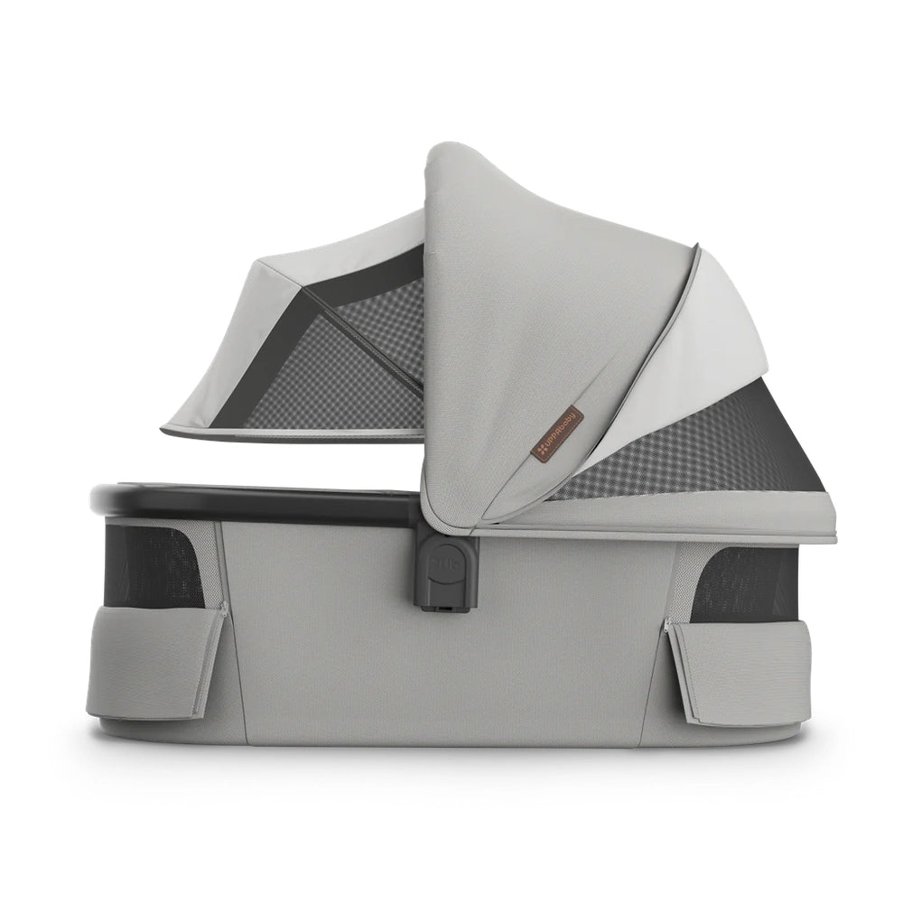 Uppababy Bassinet V3 in gray with canopy and side pockets, mounted on stroller frame for newborn transport.