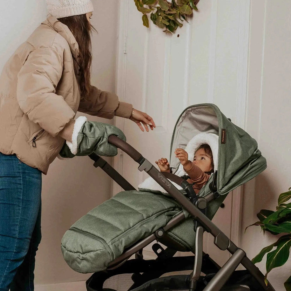 UPPABABY Cozy Ganoosh stroller footmuff in green keeps baby warm as parent pushes and adjusts the stroller.