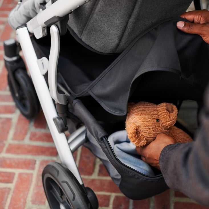 Uppababy Cruz V2 basket cover on stroller with a plush brown teddy bear tucked inside