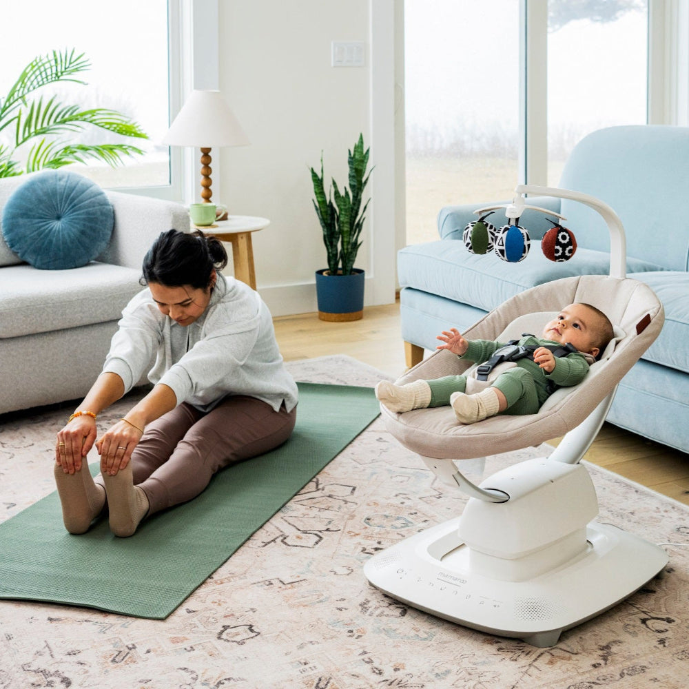 Uppababy Mamaroo Smart Swing with beige seat and colorful overhead toy bar in a cozy living room