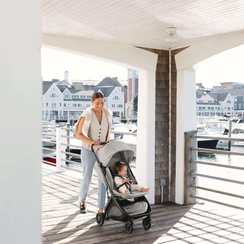 Uppababy Minu V3 stroller in gray fabric with baby seated on a marina boardwalk