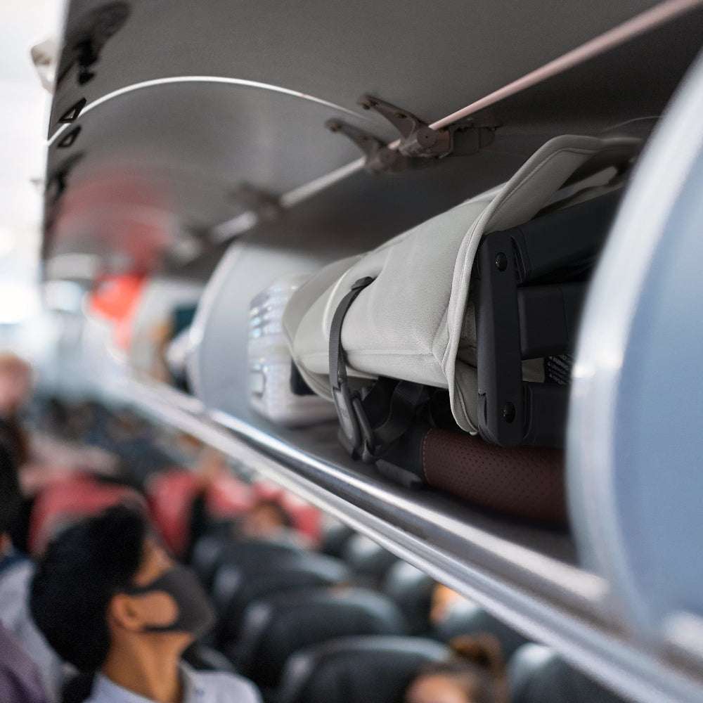 Uppababy Minu V3 stroller folded in airplane overhead bin; compact gray travel stroller