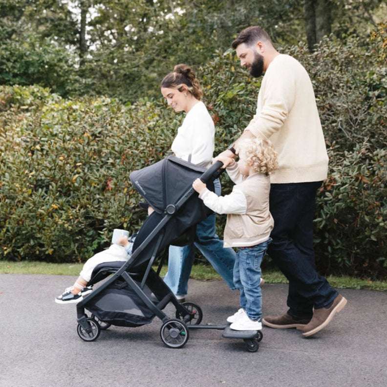 UPPABABY Piggyback ride-on board for Minu stroller; toddler stands on board as parents walk
