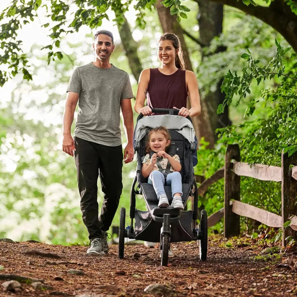 Uppababy Ridge Stroller pushed along a forest trail by a smiling mom, gray seat and sturdy all-terrain wheels.