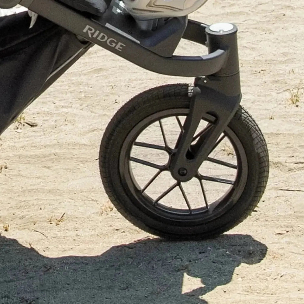 Uppababy Ridge Stroller front wheel and dark gray frame on a sandy path, showcasing rugged wheel design.