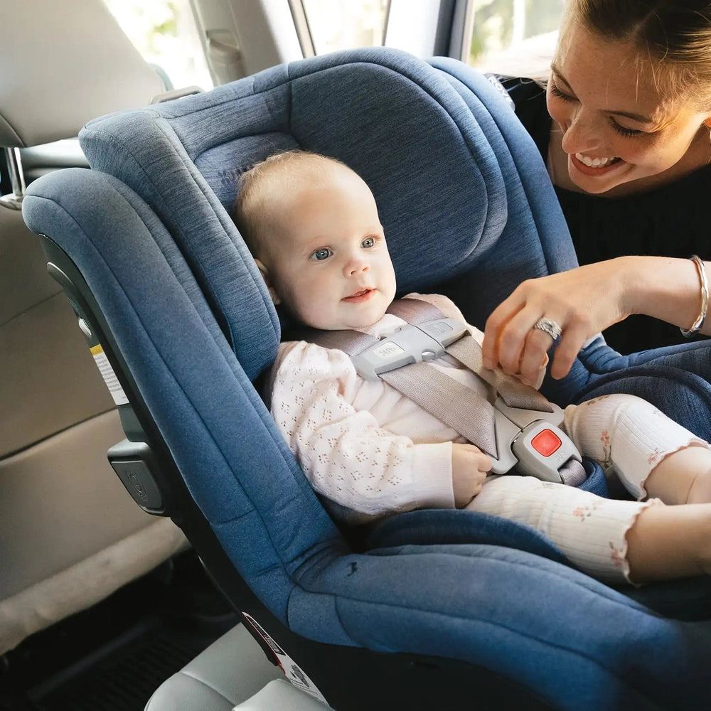 Uppababy Rove convertible car seat in blue fabric with infant secured in 5-point harness beside caregiver.