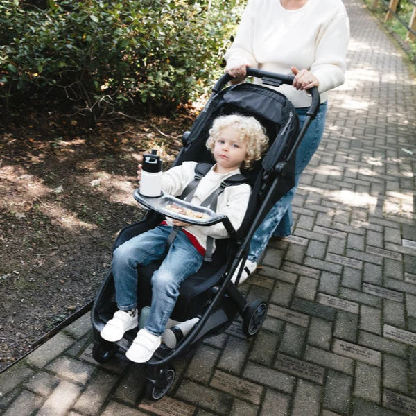 Uppababy Snack Tray for Minu V3 attached to black stroller; child seated with water bottle on tray.