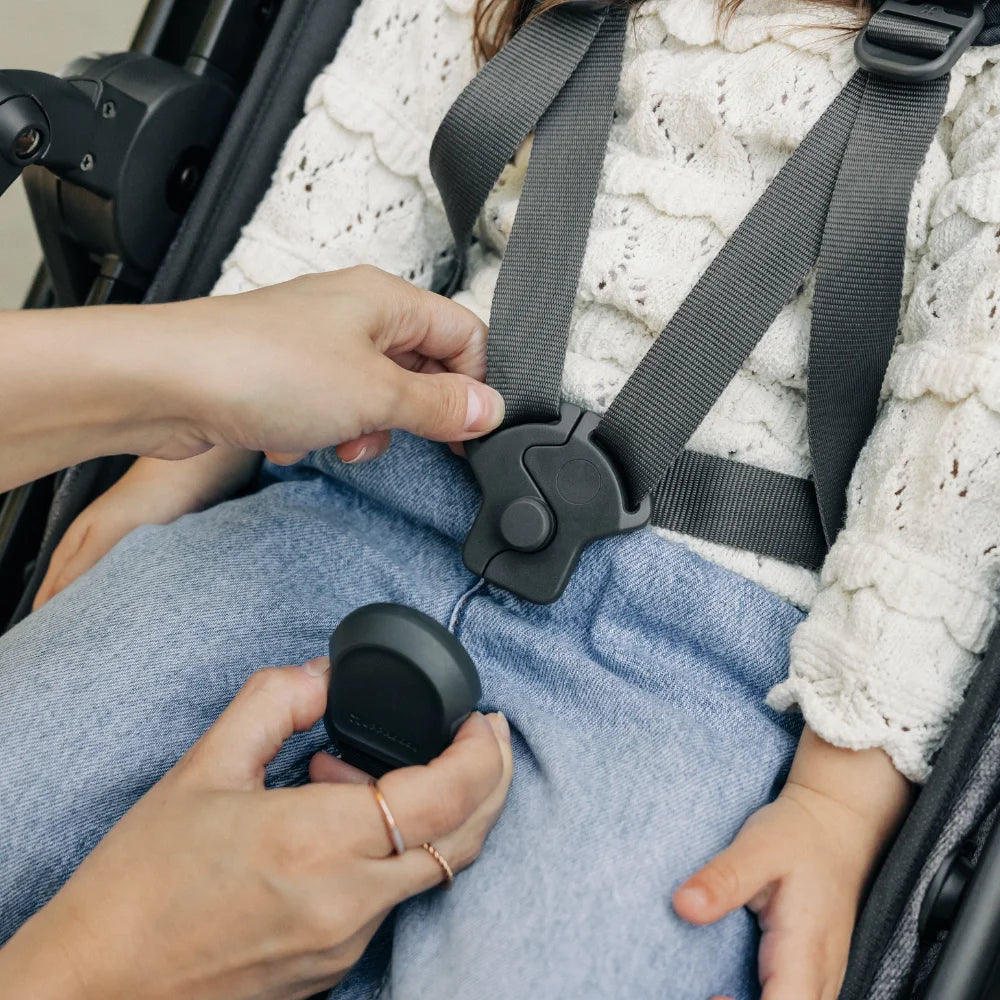 Uppababy Vista V3 Stroller; caregiver buckles the five-point harness on a child in denim jeans.