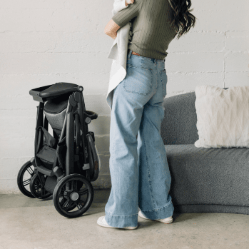 Uppababy Vista V3 Stroller folded in black beside a woman in light-wash jeans.