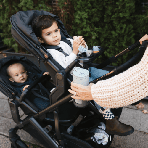 Uppababy Vista V3 Stroller with double seats; parent clips a gray cup holder as two kids ride.