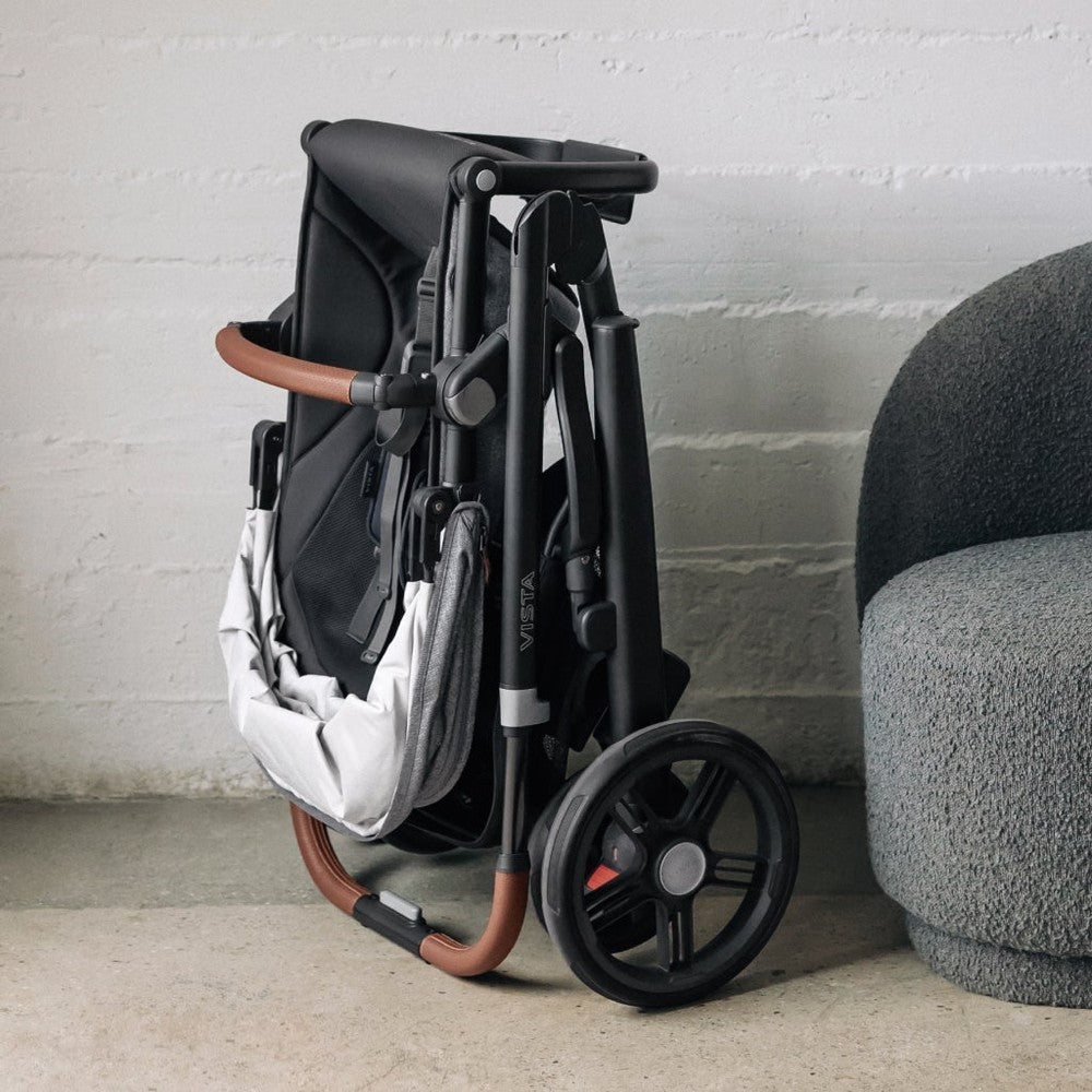 Foldable stroller with brown handles against a light gray wall.