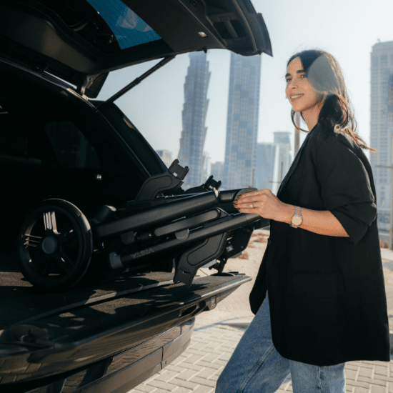 Uppababy Vista V3 Stroller folded in trunk as a woman loads it, urban city skyline behind.