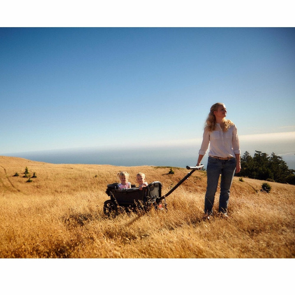 VEER All-Terrain Cruiser Wagon with two children riding in a wagon on a sunny grassy hill