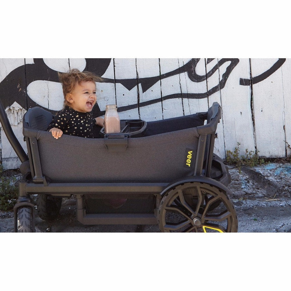 Veer All-Terrain Cruiser Wagon with toddler in dark gray chassis, yellow VEER logo, large wheels