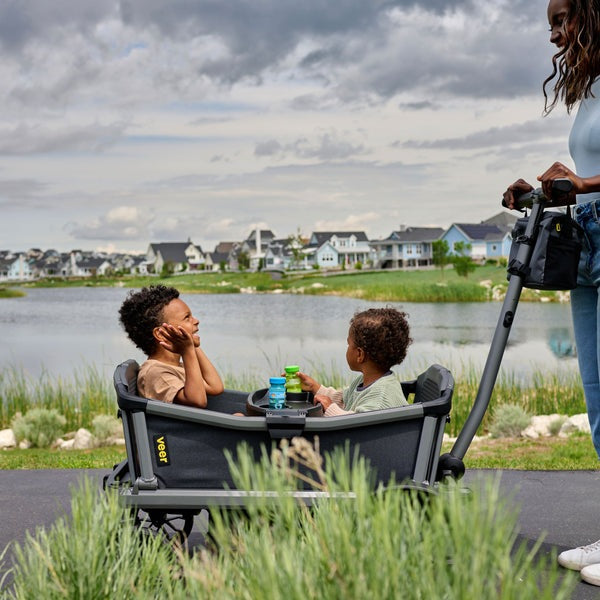 Veer City Cruiser Wagon in gray with two kids seated inside, pulled by an adult along a lakeside path