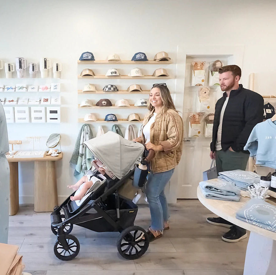Two people shopping in a store with baby stroller and clothing items.