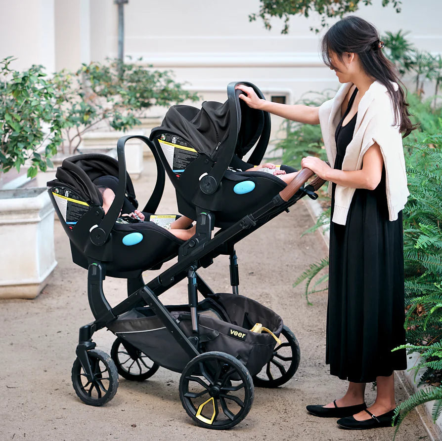 Woman adjusting a stroller with car seats in an outdoor setting