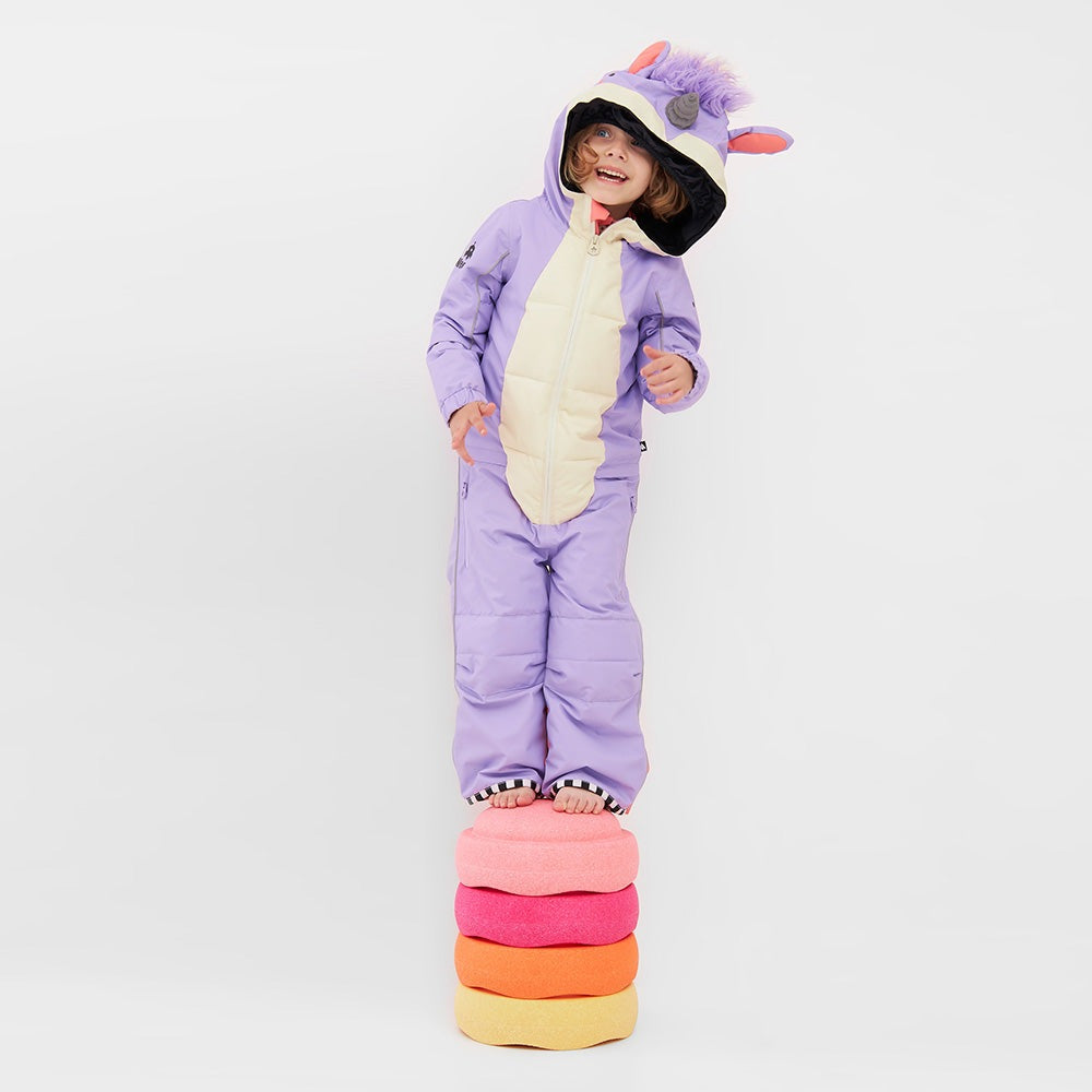 Weedo Lila Unicorn Snowsuit for toddlers, lavender with cream front and hood ears, child stands on stacked cushions