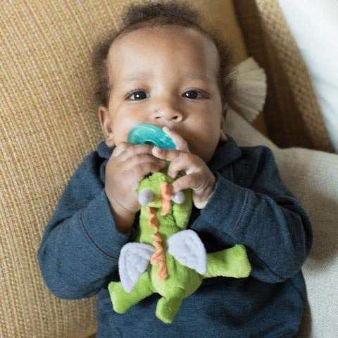 WubbaNub Infant Plush Toy Pacifier Fairytale Dragon by Aurora; baby holds teal pacifier with dragon plush.