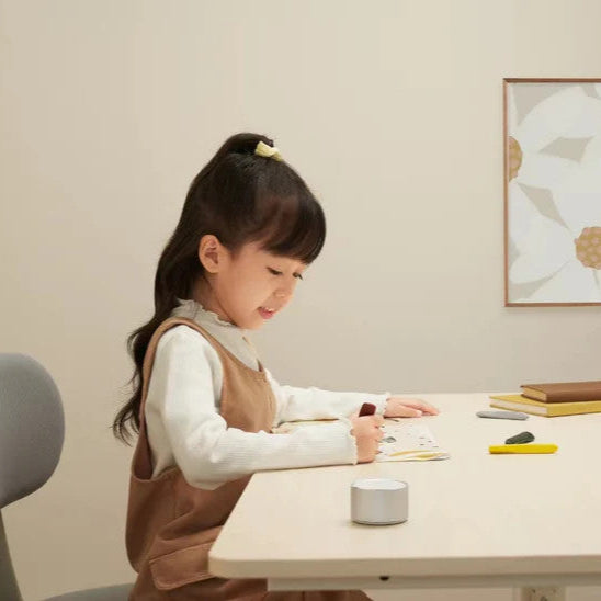 Yeelight Natural Light Floor Lamp, white minimalist cylindrical design on a desk beside a girl drawing.