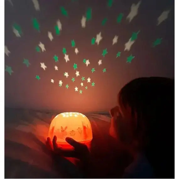A Little Lovely Company Projector Night Light glows orange as a child holds it, projecting green and white stars on the ceiling.