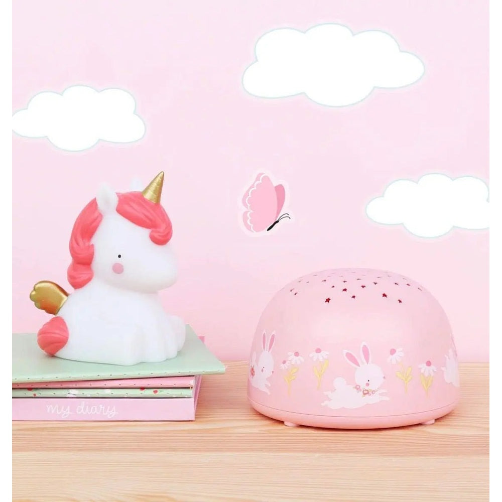 A Little Lovely Company projector night light set featuring a white unicorn and pink bunny motifs on a wooden desk.