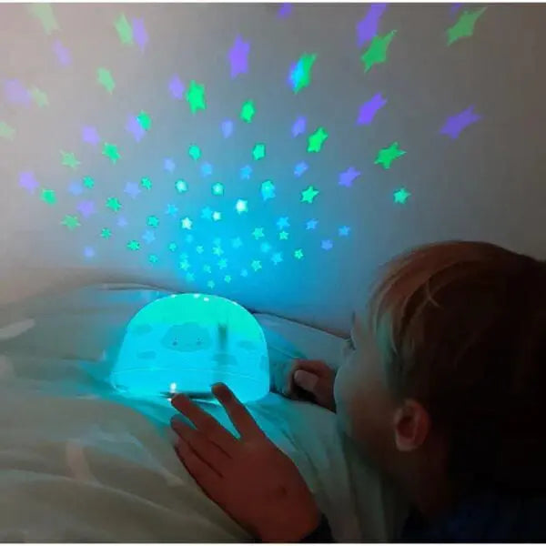 A Little Lovely Company Projector Night Light casts blue-green stars on the ceiling as a child watches.