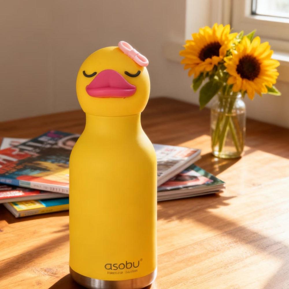 Yellow duck-shaped water bottle with a pink bow on a wooden table with sunflowers in the background.