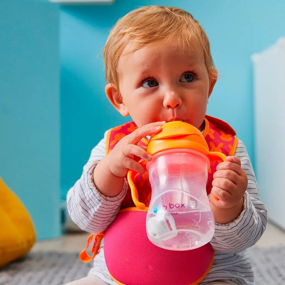 B.Box New Sippy Cup Matte Edition, pink matte body with orange lid/handles, baby sipping from it.