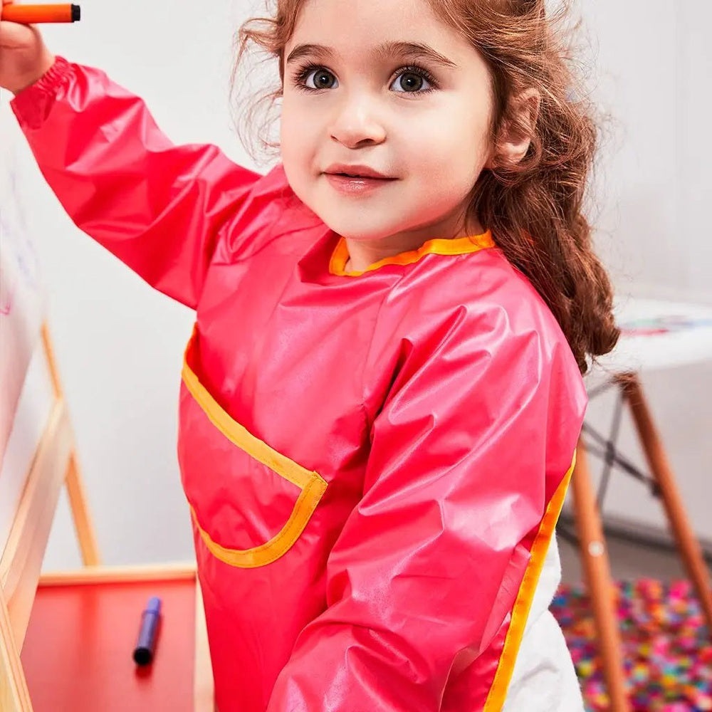 B.BOX Smock Bib (6M-2Y) pink waterproof bib with yellow trim pocket, a girl drawing with a marker.