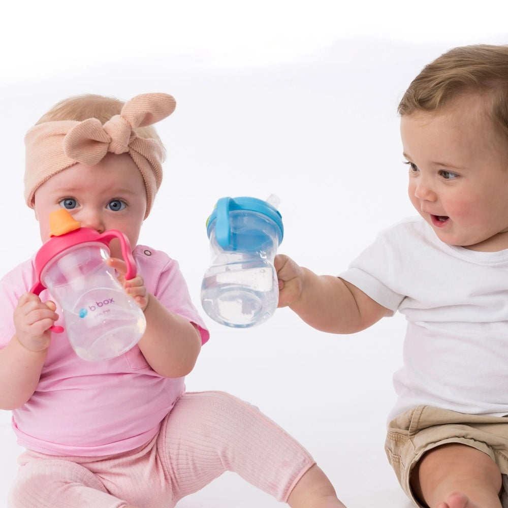 B.Box Transition Value Pack: two baby sippy cups-pink with orange spout and blue lid-held by toddlers.