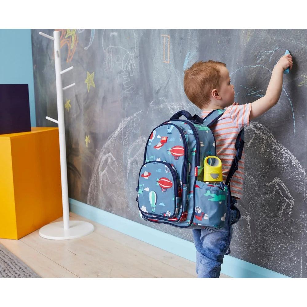 B.Box Tritan Drink Bottle with yellow lid clipped to a blue kids' backpack as a child draws on a chalkboard.