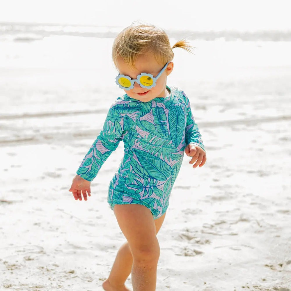 Babiators Flowers Shape Sunglasses The Wild Flower: child walks on a sunny beach wearing blue flower frames with yellow mirrored lenses.