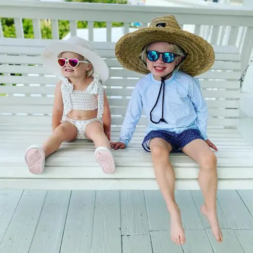 Babiators Heart Shape Polarized Sunglasses Pink worn by smiling kids on a sunny bench, showcasing pink heart frames.