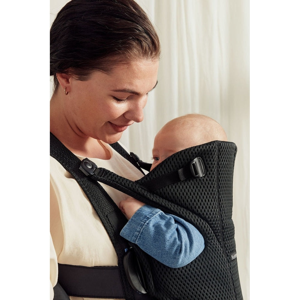 BabyBjorn Baby Carrier Free in black mesh, worn by a mother carrying her infant close to her chest with padded straps.