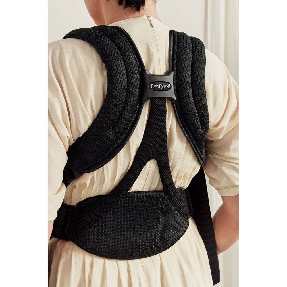 BabyBjorn Baby Carrier Free worn on a beige dress; ergonomic padded straps and waist belt secured around the back.