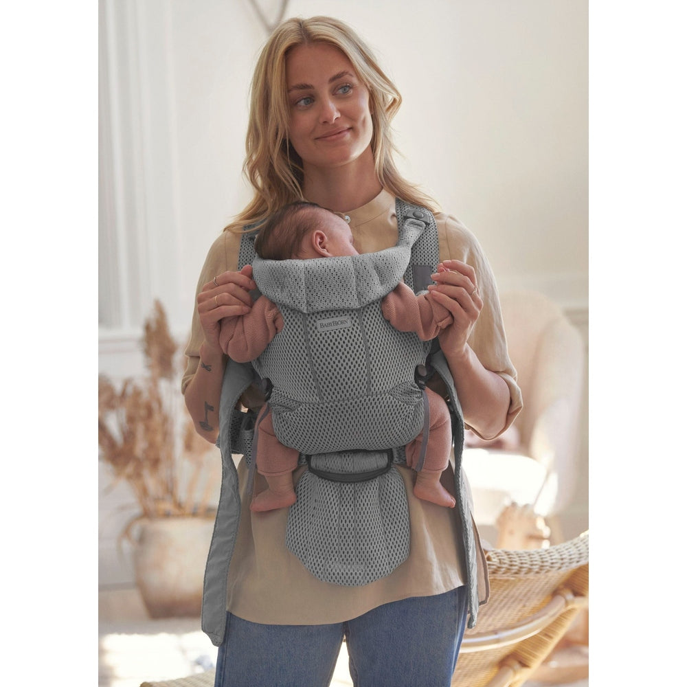 Mother wearing BABY BJORN Baby Carrier Free in gray mesh, securely holding a newborn in a cozy home setting.