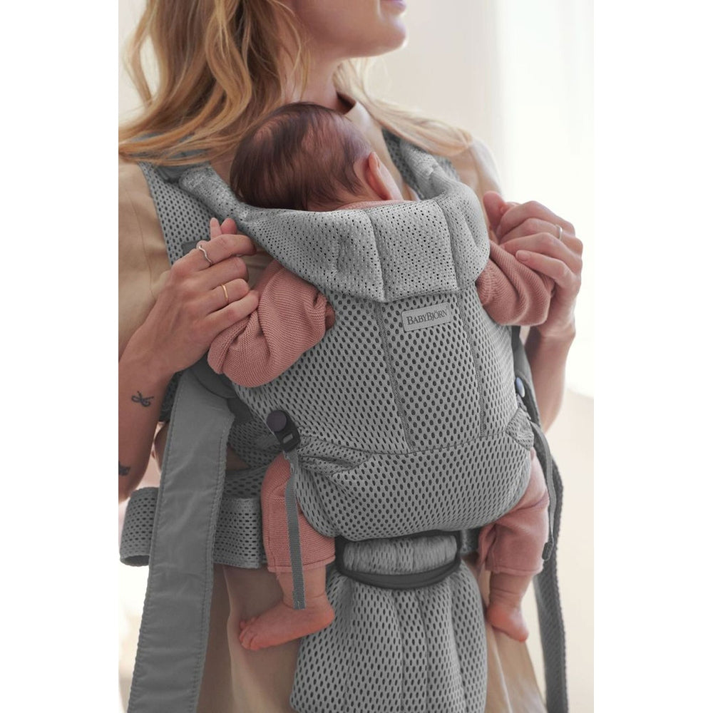 BabyBjorn Baby Carrier Free in grey mesh, worn by a mother with an infant resting snug against her chest; logo visible.